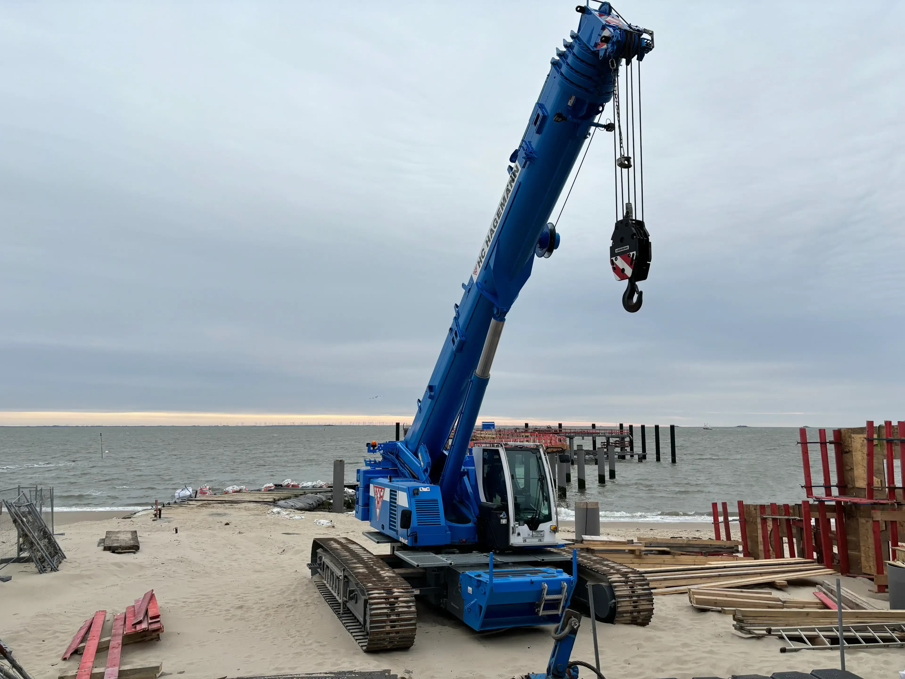 Blauer Raupenkran mit Teleskopausleger bei Kuestenschutzarbeiten am Strand