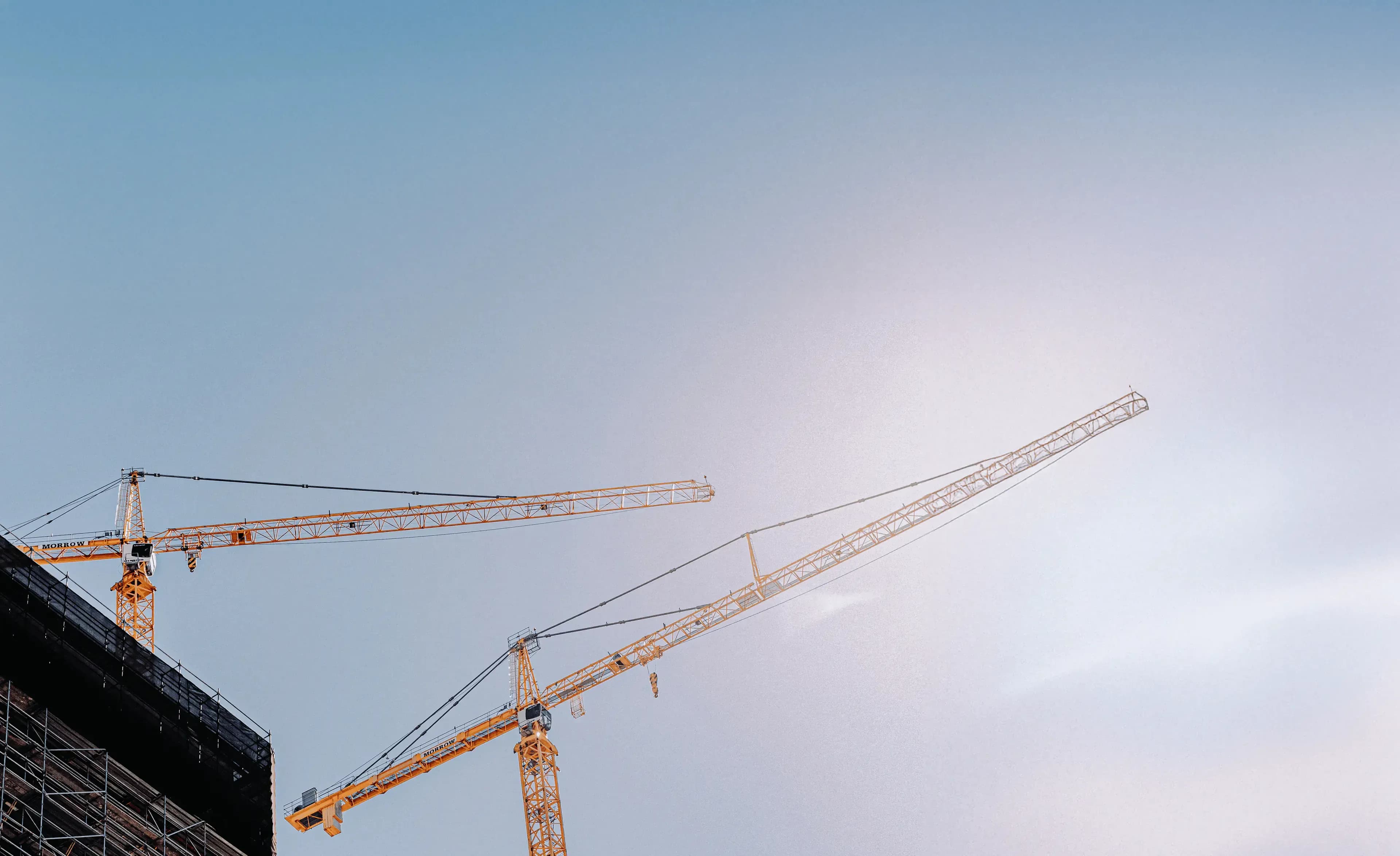 Zwei Turmkrane als Silhouette vor goldenem Abendhimmel auf Grossbaustelle